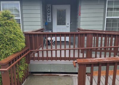 A gray house with a wooden accessible ramp leading to a white front door. A "HOME" sign is displayed near the door.