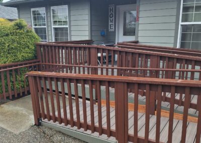 A grey house with white trim features a wooden wheelchair ramp leading to the front door. A sign with the word "HOME" hangs beside the entryway.